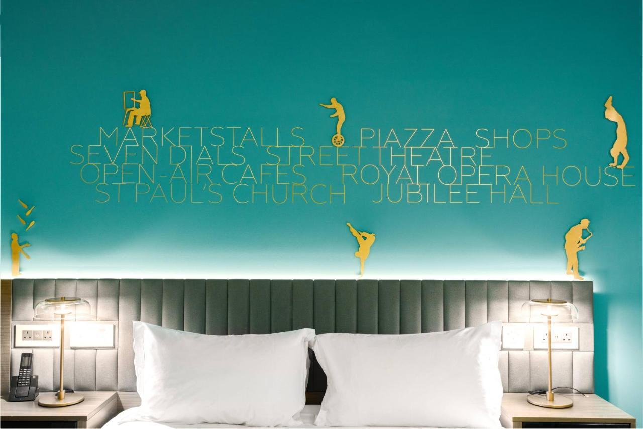 Middle Eight - Covent Garden - Preferred Hotels And Resorts Λονδίνο Εξωτερικό φωτογραφία The photo shows a modern hotel room with a distinctive turquoise wall. On the wall, there are gold silhouettes of people engaged in various activities, suggesting movement or leisure. The wall also features text that highlights local attractions like