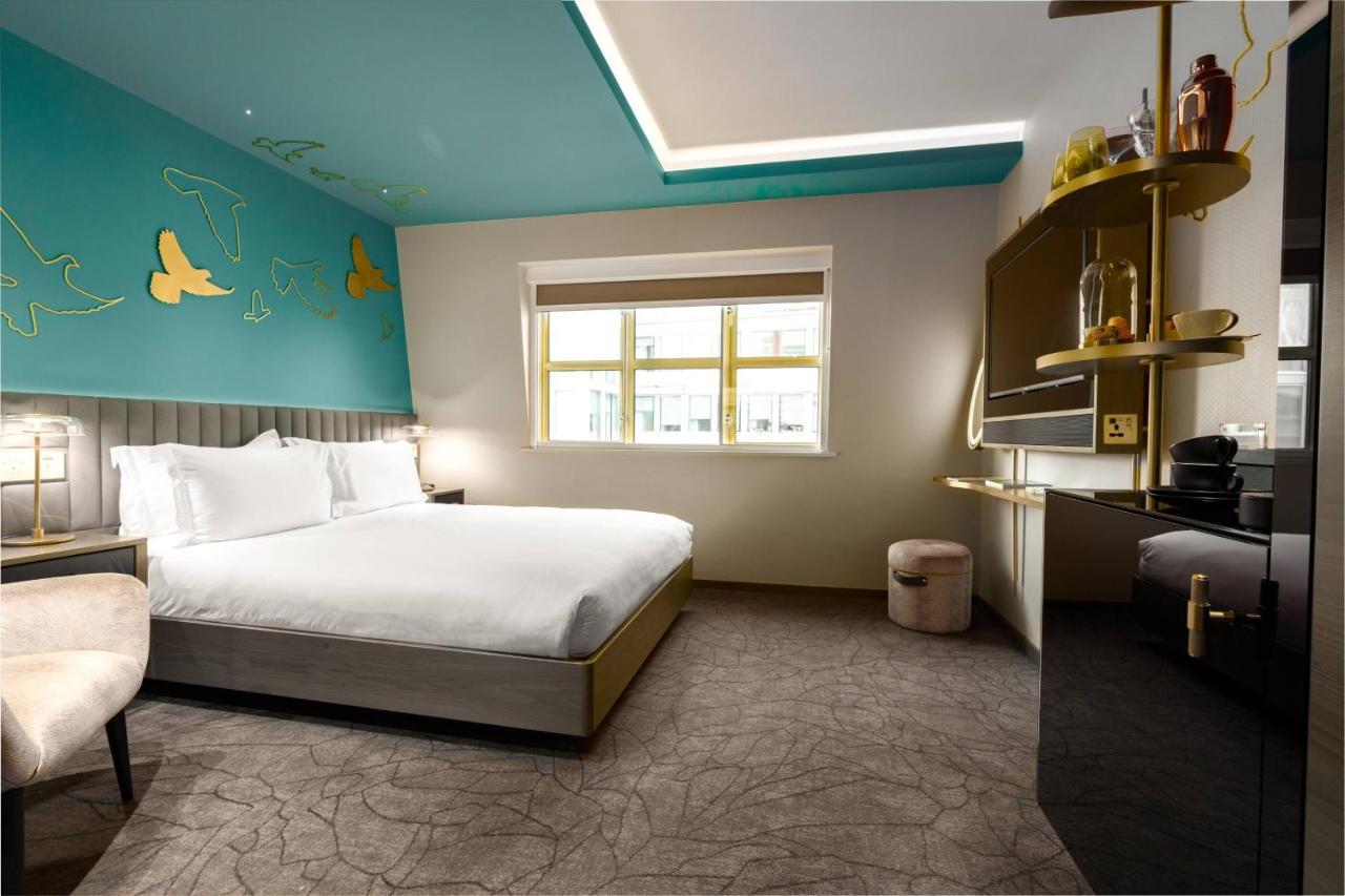 Middle Eight - Covent Garden - Preferred Hotels And Resorts Λονδίνο Εξωτερικό φωτογραφία The photo shows a modern hotel room featuring a large bed with white linens positioned against a wall. The decor includes a striking turquoise ceiling and decorative elements, such as yellow motifs, on the wall. There are large windows allowing natur