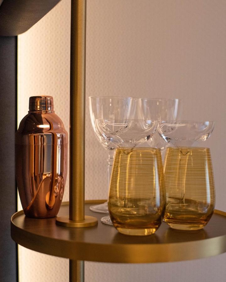 Middle Eight - Covent Garden - Preferred Hotels And Resorts Λονδίνο Εξωτερικό φωτογραφία The photo shows a stylish bar setup featuring a shiny copper cocktail shaker positioned next to several elegant glassware pieces. There are four tall, clear stemmed glasses and two round, amber-colored glasses with a textured pattern. The background 