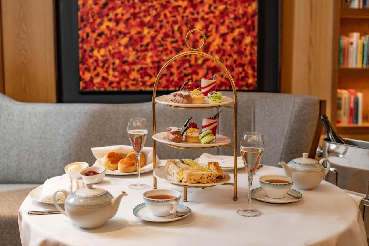 Middle Eight - Covent Garden - Preferred Hotels And Resorts Λονδίνο Εξωτερικό φωτογραφία The photo shows an elegant afternoon tea setup on a white tablecloth. At the center, there is a multi-tiered stand displaying a variety of pastries and desserts, including cakes and colorful sweets. Surrounding the stand are teapots and teacups, read