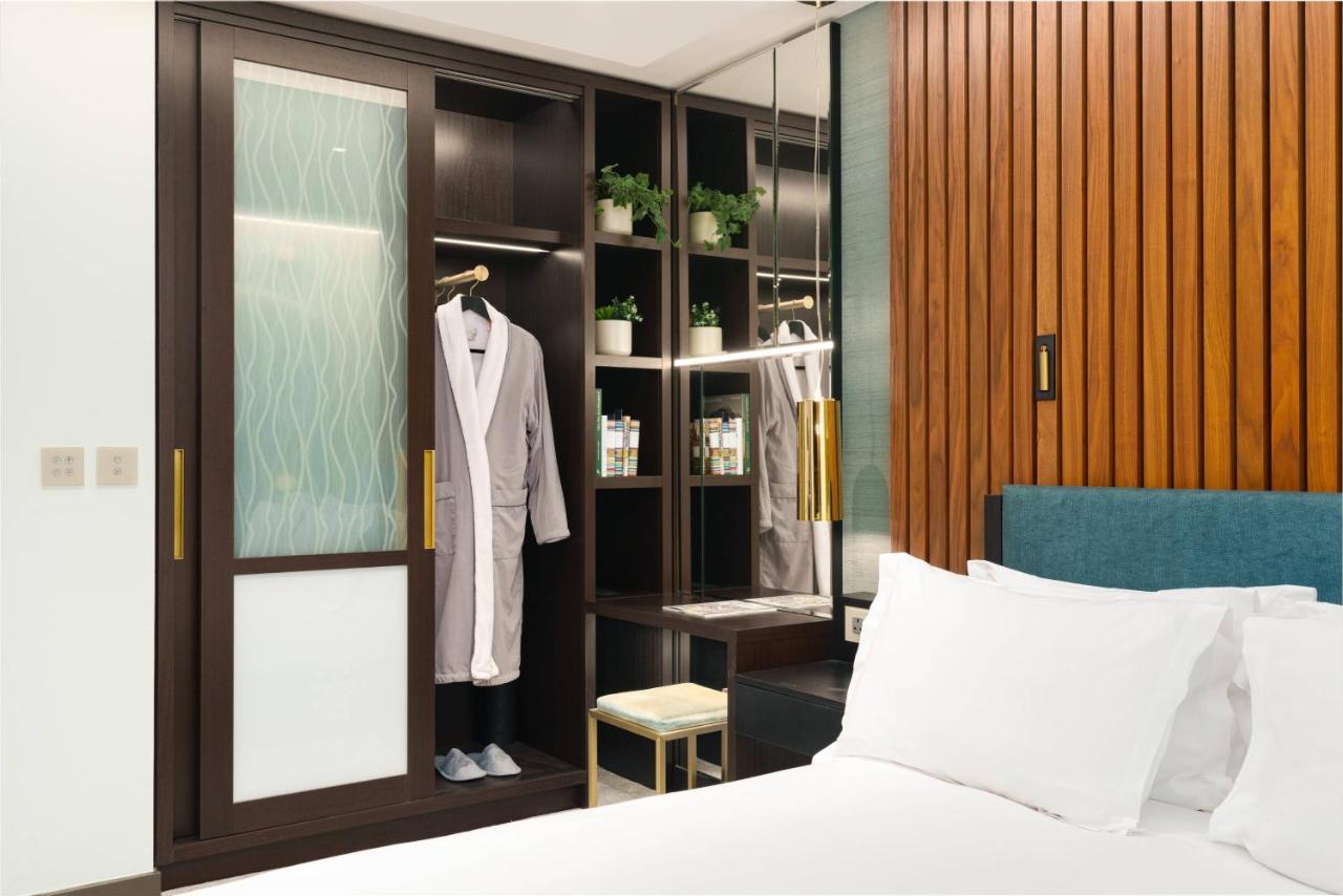 Middle Eight - Covent Garden - Preferred Hotels And Resorts Λονδίνο Εξωτερικό φωτογραφία The photo shows a cozy hotel room featuring a neatly made bed with white bedding. On the side, there is a wardrobe with sliding glass doors. Inside the wardrobe, a light-colored robe is hanging, and there are shelves with small plants and toiletries 
