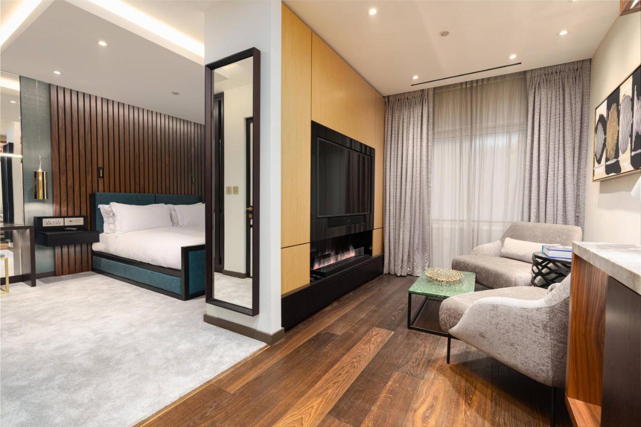 Middle Eight - Covent Garden - Preferred Hotels And Resorts Λονδίνο Εξωτερικό φωτογραφία The photo depicts a modern hotel room or suite featuring a cozy living space. On one side, there's a comfortable bed with plush bedding, positioned against a backdrop of elegant wooden paneling. Adjacent to the bed is a contemporary fireplace integra