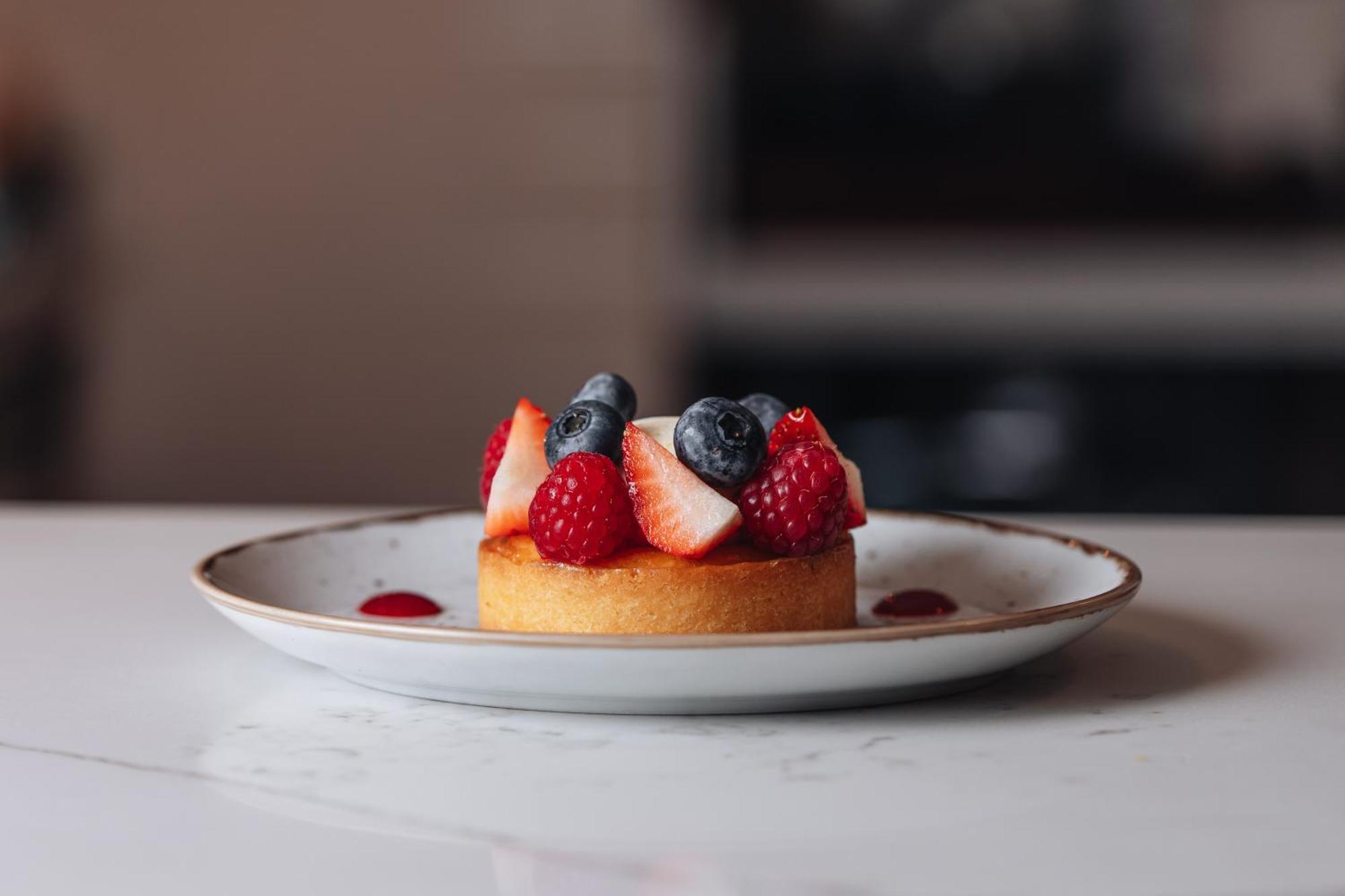 Middle Eight - Covent Garden - Preferred Hotels And Resorts Λονδίνο Εξωτερικό φωτογραφία The photo shows a delicious-looking dessert on a white plate. The dessert appears to be a small tart or cake topped with fresh strawberries, raspberries, and blueberries. It has a golden crust, and there are small dollops of a red sauce or fruit pure