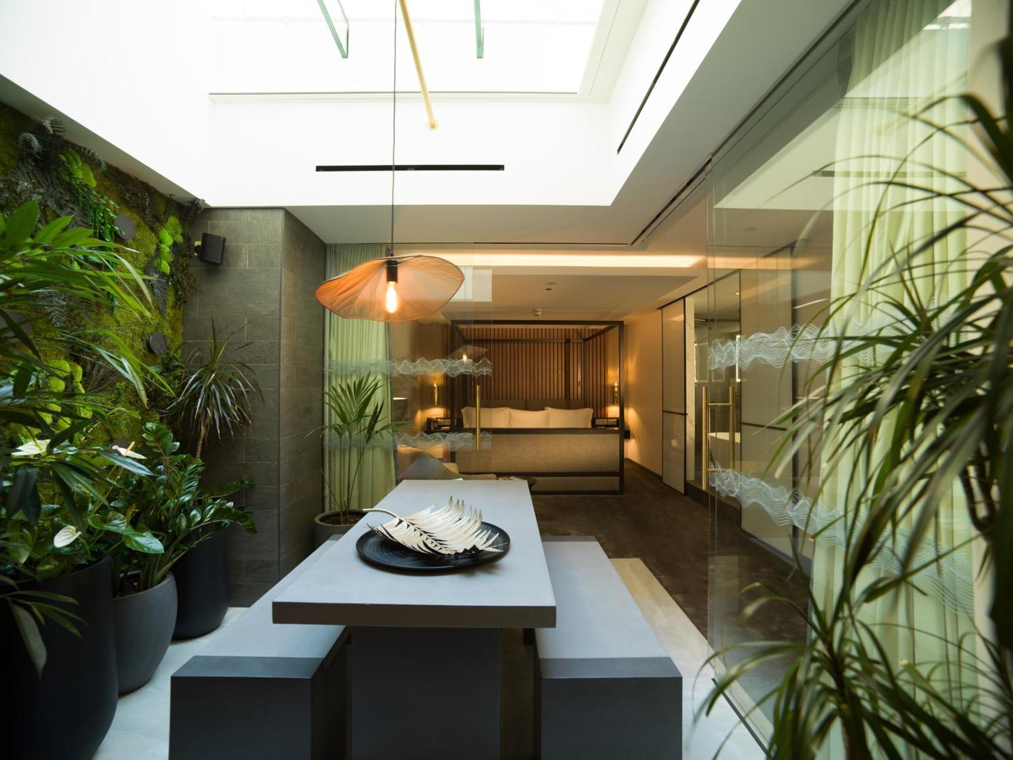 Middle Eight - Covent Garden - Preferred Hotels And Resorts Λονδίνο Εξωτερικό φωτογραφία The photo depicts a modern, airy interior space that features a dining area. The dining table is rectangular and made of a light-colored material, paired with simple benches on either side. Above the table, there is a stylish pendant light, providing